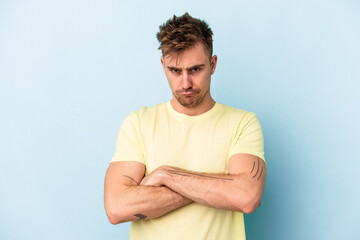 Young caucasian man isolated on blue background frowning face in displeasure, keeps arms folded.