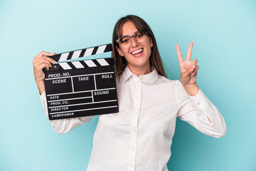 Wall Mural - Young caucasian woman holding clapperboard isolated on blue background showing number two with fingers.