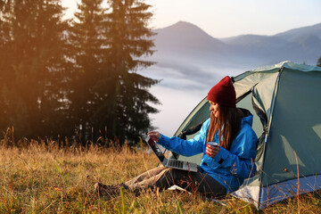 woman working on laptop near camping tent outdoors surrounded by beautiful nature