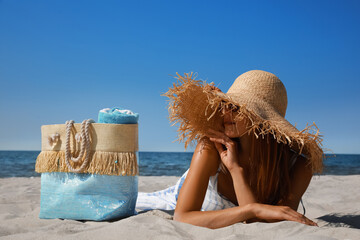 Sticker - Woman with beach bag and straw hat lying on sand near sea