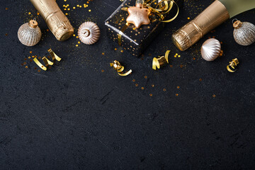 Wall Mural - Christmas or New Year concept. Holiday gift box or present with ribbon, champagne, golden confetti and gold baubles on black background.  Christmas  card. Christmas Decoration. Mock up. Top view.