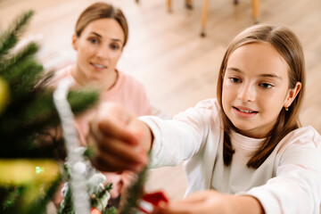 White mother and daughter smiling while decorating christmas tree