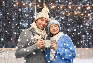 Wall Mural - winter holidays, christmas and love concept - happy romantic couple in knitted hats and scarves with mugs over ice rink background