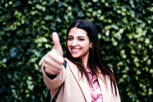 Smiling Businesswoman Showing Thumbs Up In Front Of Ivy Plants