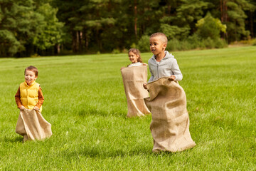 Wall Mural - childhood, leisure and people concept - group of happy little children playing bag jumping game at park