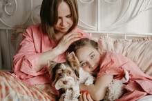 Mother And Daughter Relaxing With Dog On Bed At Home