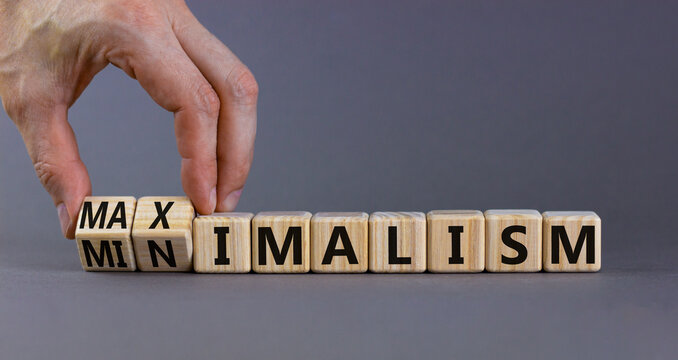 Minimalism or maximalism symbol. Businessman turns wooden cubes and changes the word minimalism to maximalism. Beautiful grey background. Business, minimalism or maximalism concept. Copy space.