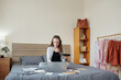 © DragonImages - Pretty smiling woman sitting on bedroom in her apartment, eating food and working with reports and docuemnts on laptop