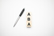 aba is made up of wooden cubes that stand on a burgundy notebook near the pen. Business concept