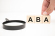 aba text wooden cube blocks and hand holding magnifying glass on table background.