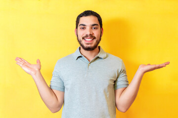 Happy young man pointing with hands to both side, isolated on yellow wall.