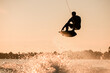 © fesenko - Beautiful silhouette of male rider holding rope and making extreme jump on wakeboard over splashing water.