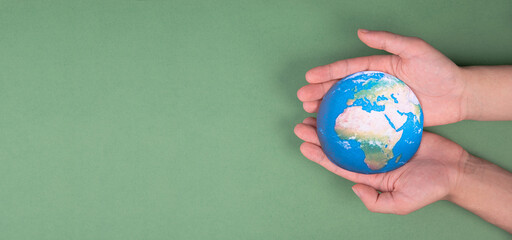 Hands holding planet earth in front of a green background, environmental isuues, copy space