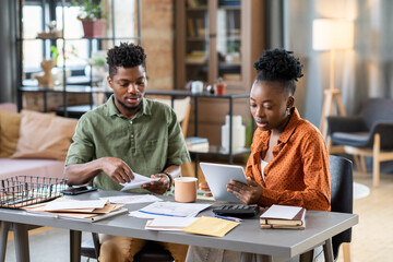 Poster - Concentrated young African American couple sitting at table with bills and analyzing month expenses at home