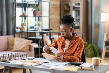 Poster - Serious young African American woman sitting at table and receiving notification about overdue payment at home