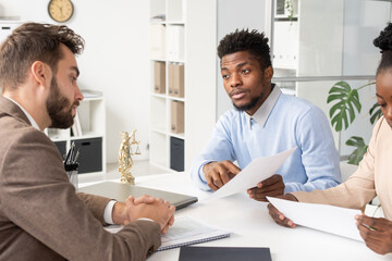 Poster - Young African American man in blue sweater pointing at contract point while asking lawyer about it at consultation
