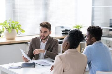 Poster - Young bearded lawyer examining contract or tax paper while giving consultation to young couple