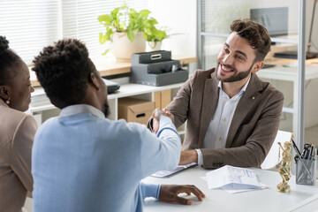 Poster - Smiling young bearded banking specialist making handshake of blackman while greeting couple in office