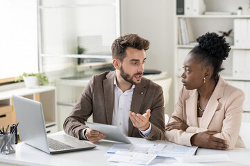 Poster - Young bearded manager using tablet while discussing income of company with colleague