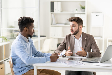 Poster - Handsome young businessman talking to African American accountant while preparing financial report with him