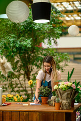 Wall Mural - Florist talking with client on the smartphone and taking an order in a flower shop