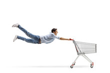 Full Length Shot Of A Casual Young Man Flying And Holding An Empty Shopping Cart