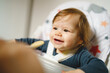 © Miljan Živković - One small caucasian baby feeding while sitting in the chair hand of unknown mother giving food to small seven months old infant with plastic spoon in room at home real people care concept copy space