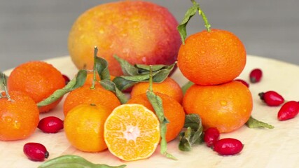 Wall Mural - Composition with sliced rotating oranges, mango, rosehip and green leaves, close up with water drops