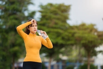 Wall Mural - tired woman drinking water after running in park