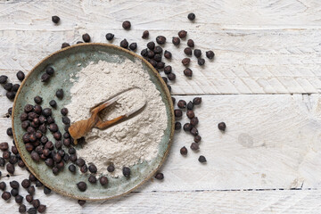 Plate and wooden scoop of black chickpea flour and beans top view