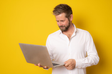 Portrait of a excited young man holding laptop computer isolated on yellow background.