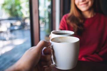 Poster - Closeup image of a man and a woman clinking coffee cups together in cafe