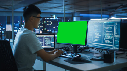 Poster - Night Office: Young Japanese Man in Working on Green Screen Chroma Key Desktop Computer. Programmer Typing Code, Creating Modern Software, e-Commerce App Design. Over Shoulder