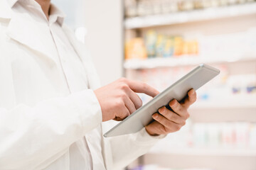 Closeup cropped image of druggist pharmacist using digital tablet for checking expiration date, side effects, active substance of drugs, pills, medicines in pharmacy