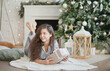 © Dina - Beautiful young woman with a gift box near christmas tree in the living room. Woman at home decorated for winter holiday season.