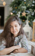 © Dina - Beautiful young woman with christmas tree in the living room at home face closeup. Cozy portrait of a woman relaxing at home.