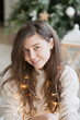 © Dina - Beautiful young woman with a gift box near christmas tree in the living room. Woman at home decorated for winter holiday season.