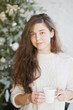 © Dina - Beautiful young woman with christmas tree in the living room at home. Woman closeup at home decorated for winter holiday season.