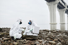 Full Length Portrait Of Two Workers Wearing Hazmat Suits Collecting Probe Samples By Water, Toxic Waste Concept, Copy Space