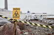 © Seventyfour - Close up of Warning Biohazard sign at ecological disaster site with people in protective suits, copy space