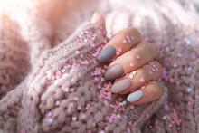 Women's Hands With A Beautiful Matte Oval Manicure In A Warm Purple Knitted Sweater And Heart Shaped Sequins. Winter Trend, Polish Beige Nails With Gel Polish, Shellac. Copy Space.