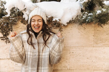 Cheerful Caucasian Young Girl Clenching Her Fists While Enjoying Good News Against Background Of Wall. Brunette Closed Her Eyes And Opened Mouth While Standing In Hat And Coat. Achievement Concept.