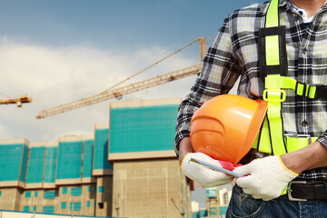 Wall Mural - close up of construction worker carrying safety helmet with crane in the background and new building site safety concept