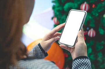 Close up women using a smartphone with an empty white screen at  Christmas festival event with pine tree.