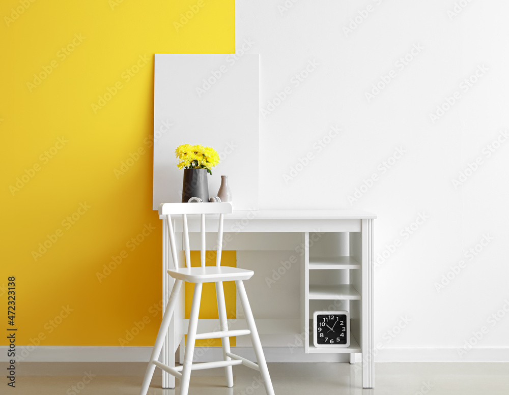 Table with flowers, headphones and blank frame near color wall