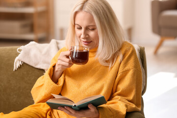 Wall Mural - Beautiful mature woman reading book and drinking tea at home on autumn day