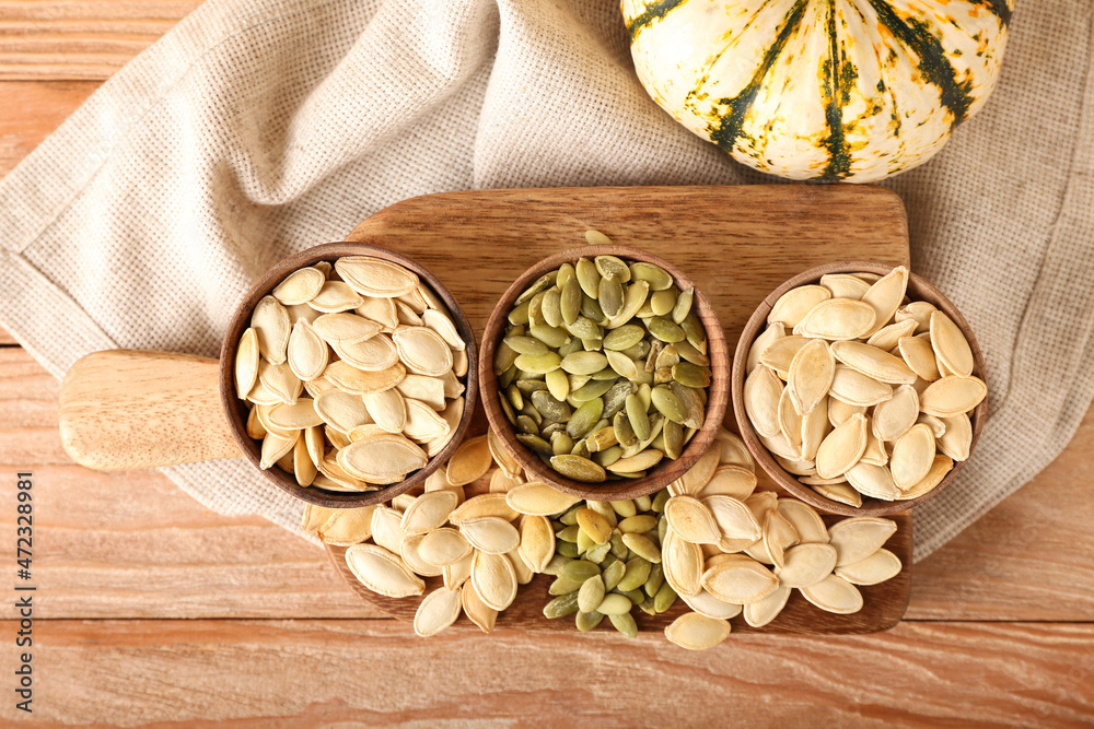 Bowls with natural pumpkin seeds on wooden background
