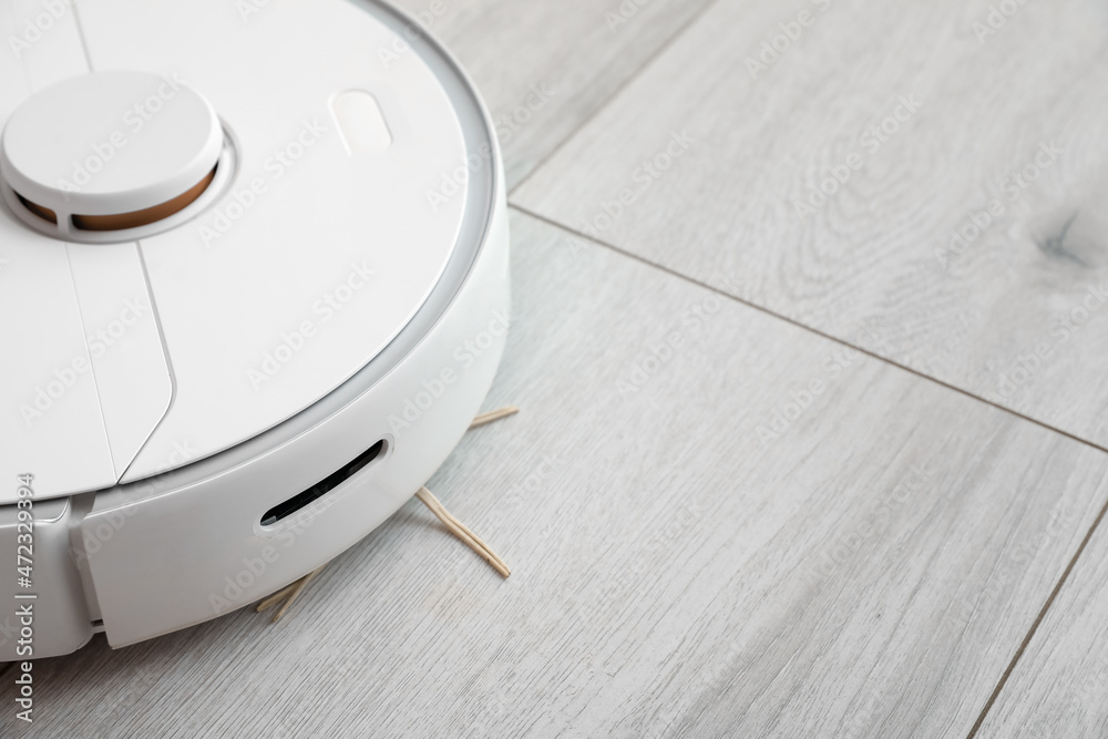 Modern robot vacuum cleaner on wooden floor in room