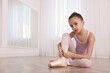 Little ballerina tying pointe shoes on floor in dance studio. Space for text