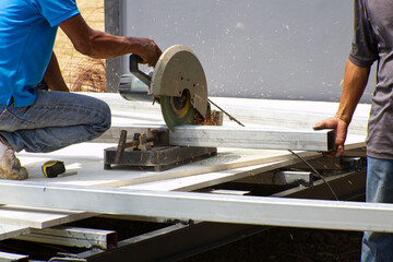 Two men are helping in cutting metal by using a metal cutting machine.  They work without any protection equipment which is quite dangerous.